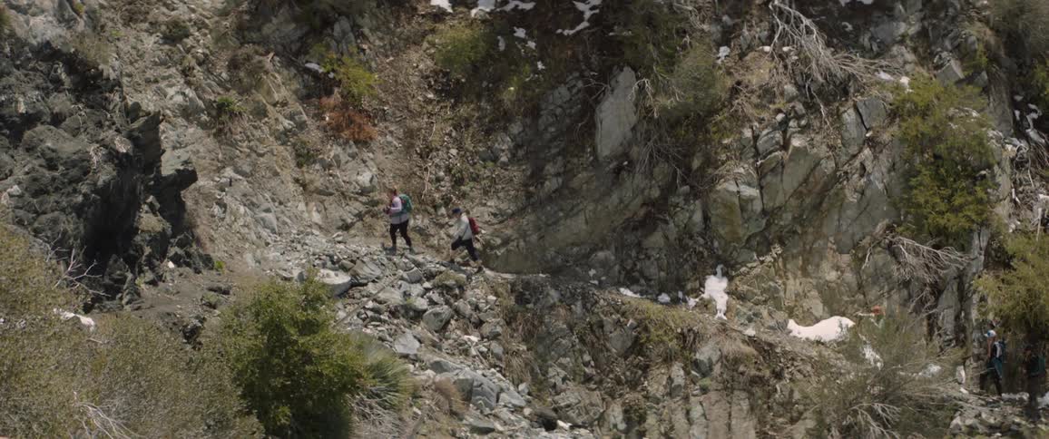 A pair of women hike along a trail leaking uphill through rocky terrain