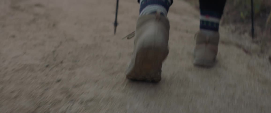Person walks along dirt trail with trekking poles