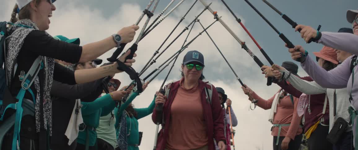 Women hold hiking sticks over other women who walk under