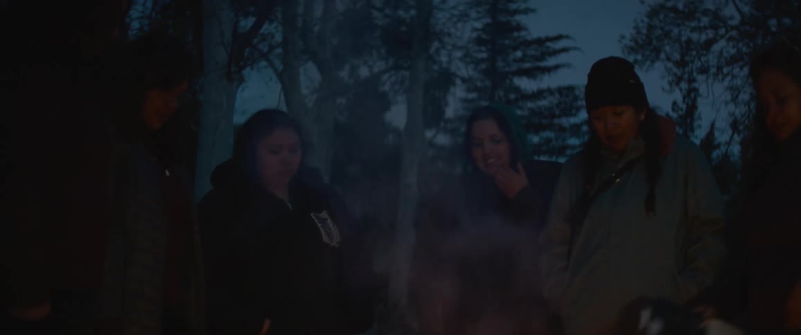 A group of women stand together around a campfire at night