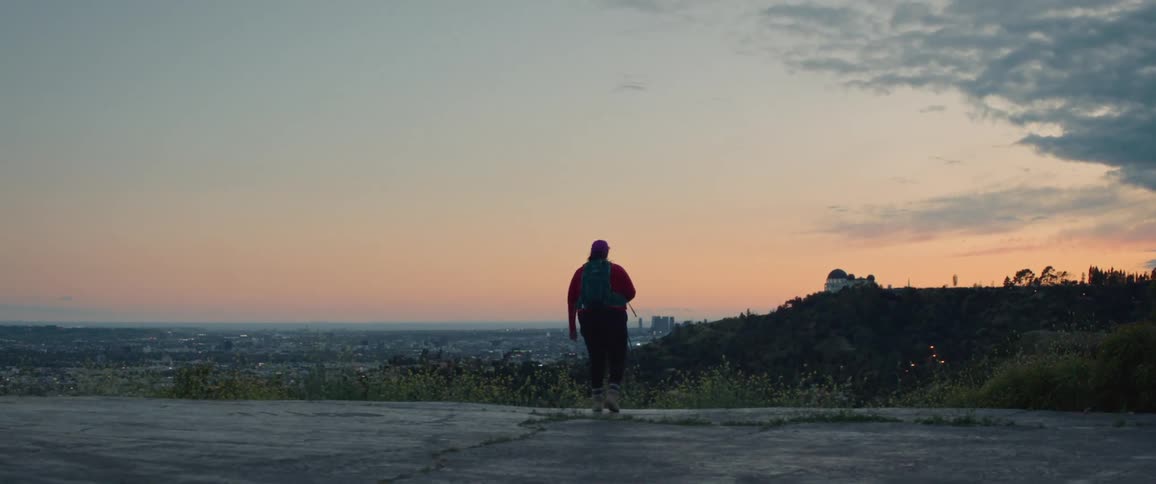 View of a woman with her back to the camera overlooking a metropolis from a hill during the dawn