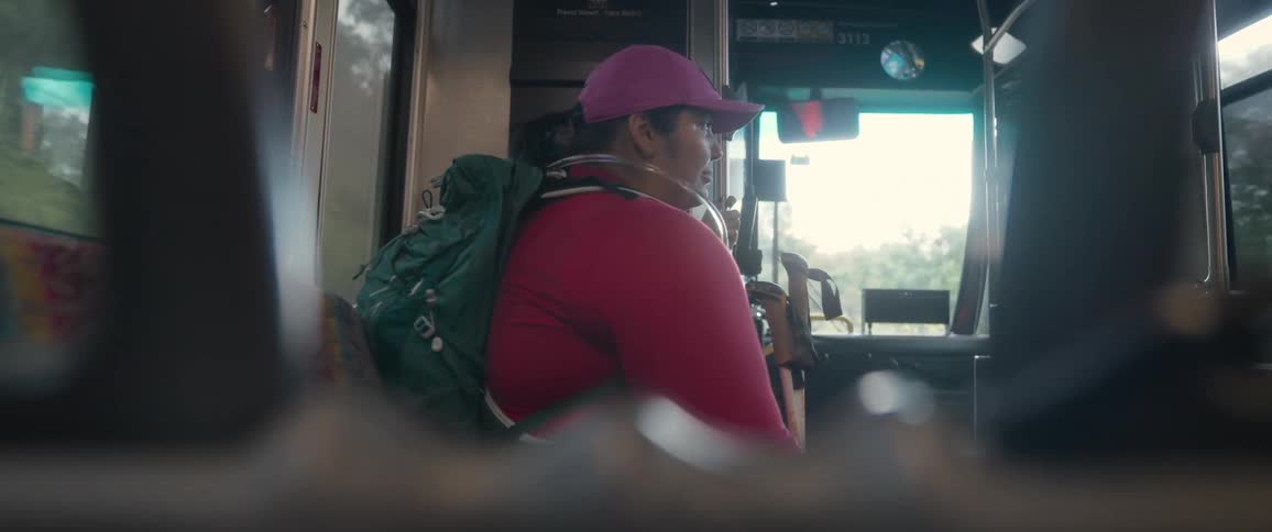 A female hiker sits on a bus while staring out the window