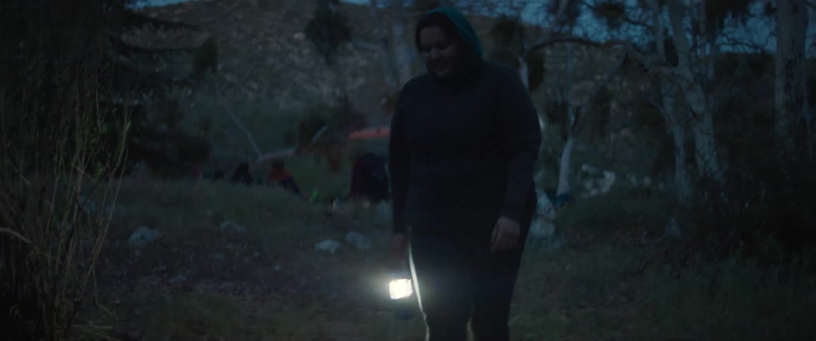 A young woman walks around a campsite while carrying a lantern at night