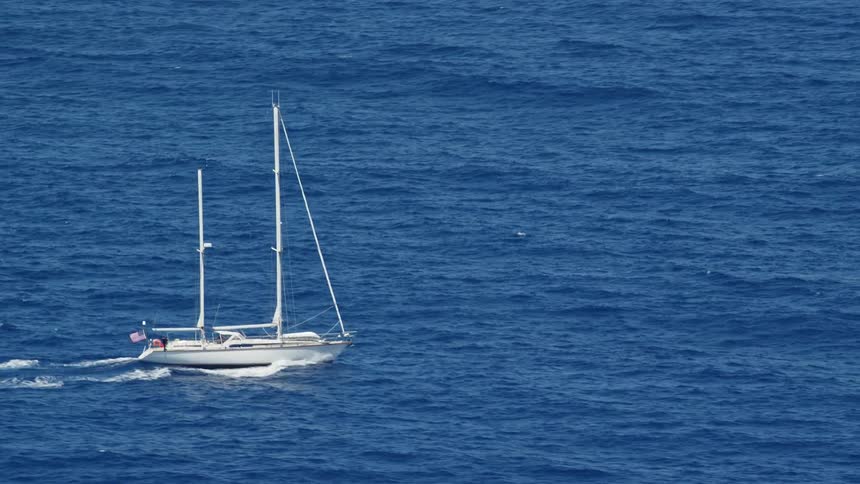 A white boat travels across the surface of the blue ocean on a sunny day