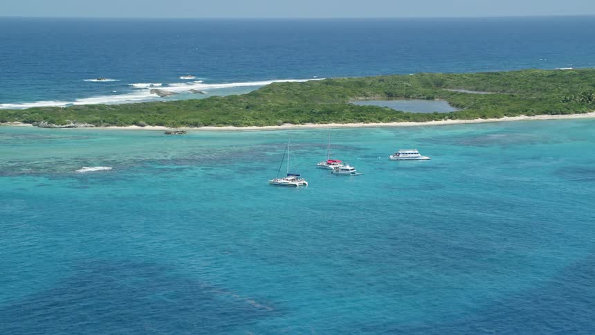 Some boats stopped next to an island with a lot of undergrowth and behind the huge ocean