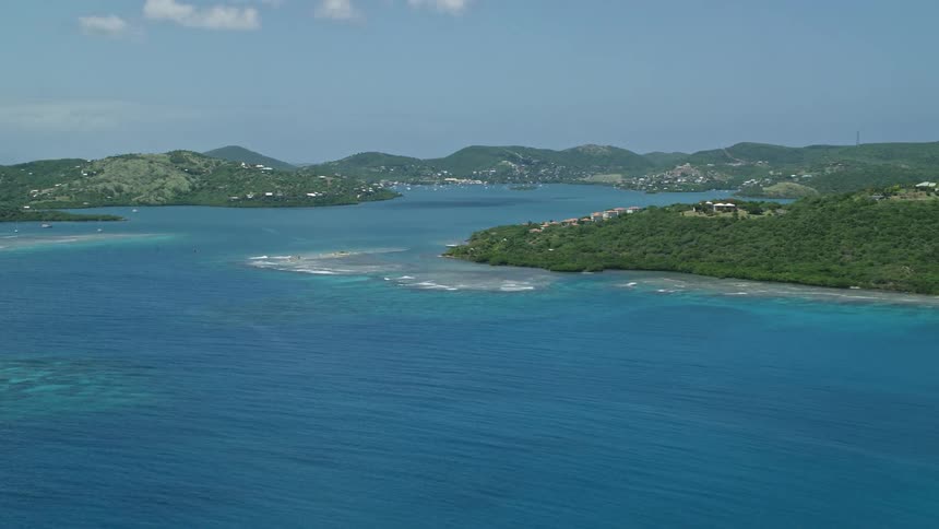 A region with several islands covered in green trees and some houses and in the middle of a bay with very blue water