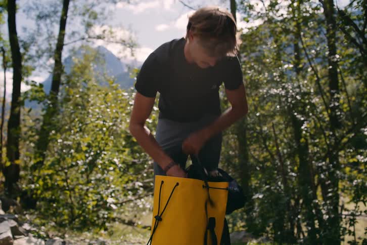 A man taking equipment out of a backpack in the forest