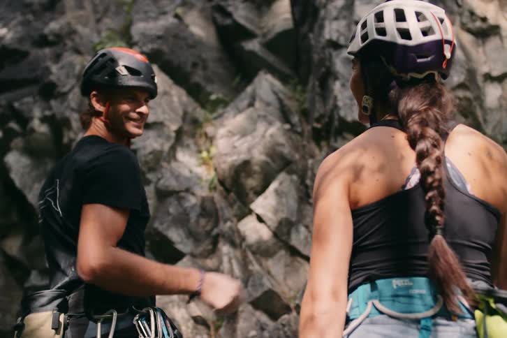 Man and woman touching hands in front of a rocky wall with climbing safety equipment