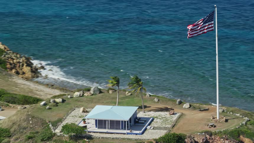 Aerial view of a house on top of a hill with an american flag on a mast next to the ocean during day time