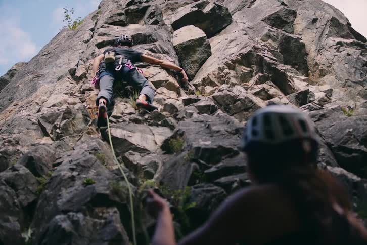 Woman assisting a man who is climbing a rocky wall of a mountain