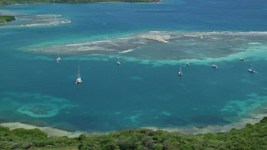 Several boats stopped in a bay of water surrounded by islands