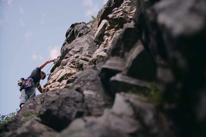 A man in safety equipment is climbing a huge rock using a rope
