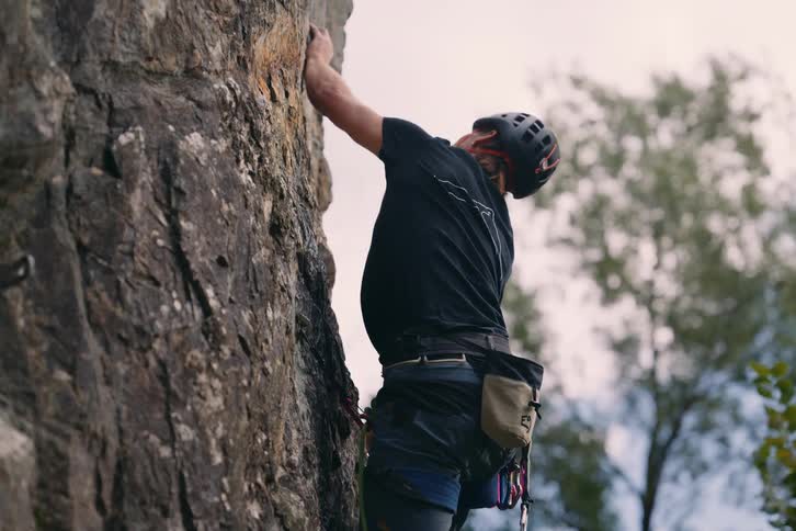 A person has their back turned and is wearing safety equipment while climbing a rock