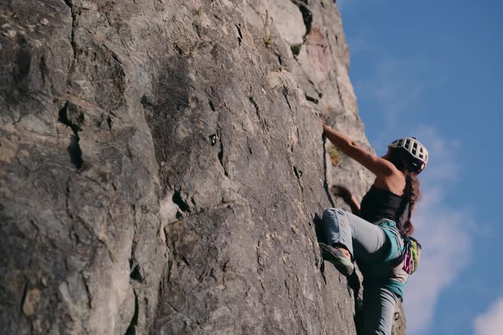 Woman wearing helmet and climbing gear clings to boulder