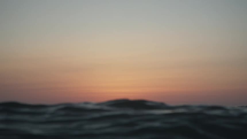 The sun is barely visible over the horizon as ocean waves rise and fall