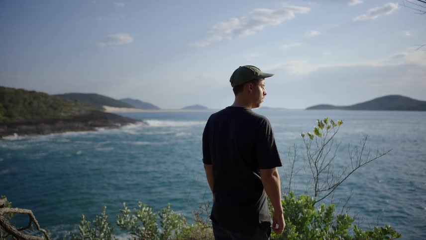 Mans back on a cliff facing the sea in slow motion