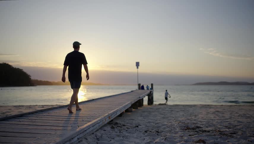 Man walking over a narrow wooden pier in the beach at sunset