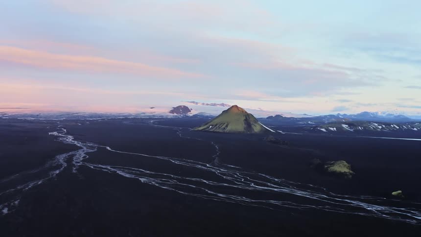Aerial of several streams running next to a volcano at sunrise