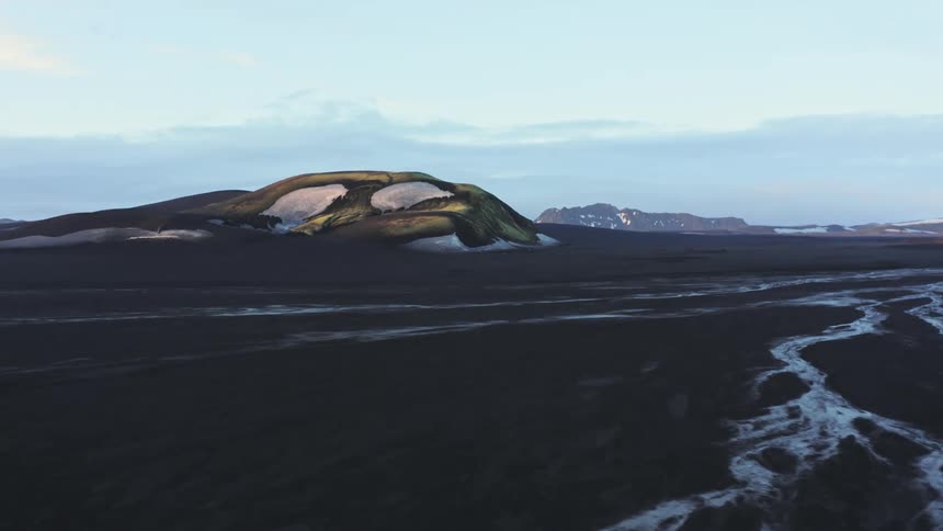 Aerial of a mountain on flat terrain with a small river