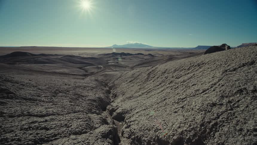 A desert region with rocks and cracks in them and in the sky the sun shining brightly