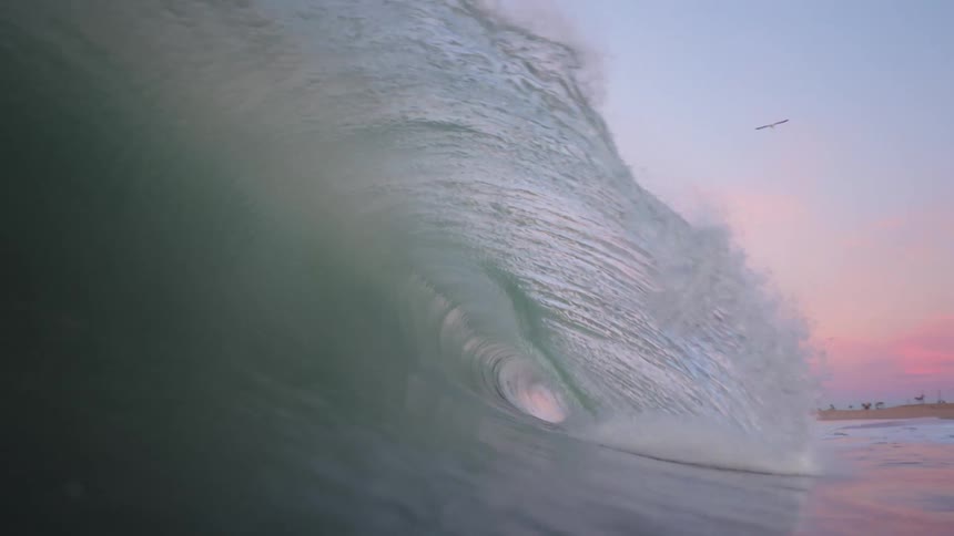 Wave crashes near shore obscuring surfer while red tints horizon