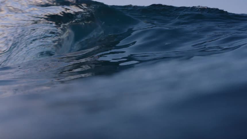 View of a wave breaking in slow motion in the sea against an orange dawn sky