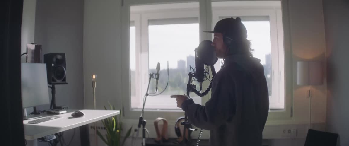 Man singing into a microphone in a home studio facing a computer