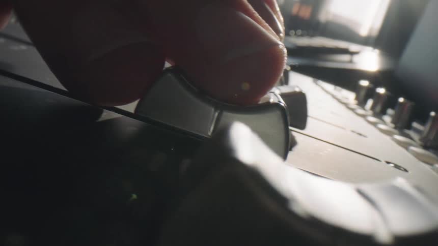 Extreme closeup of a persons finger adjusting down the electronic music mixer