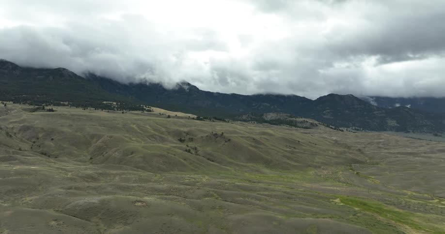 A region with a green field with many mountains and clouds behind