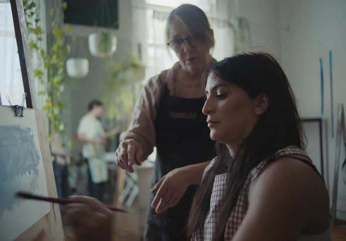 Elderly woman gives instructions to a lady painting in a studio at midday