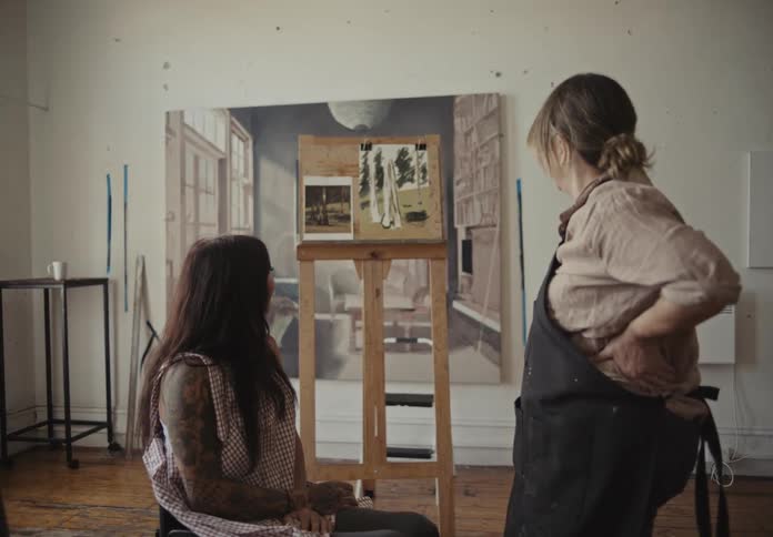 Woman talking with a wheelchair user and analyzing paintings on a canvas