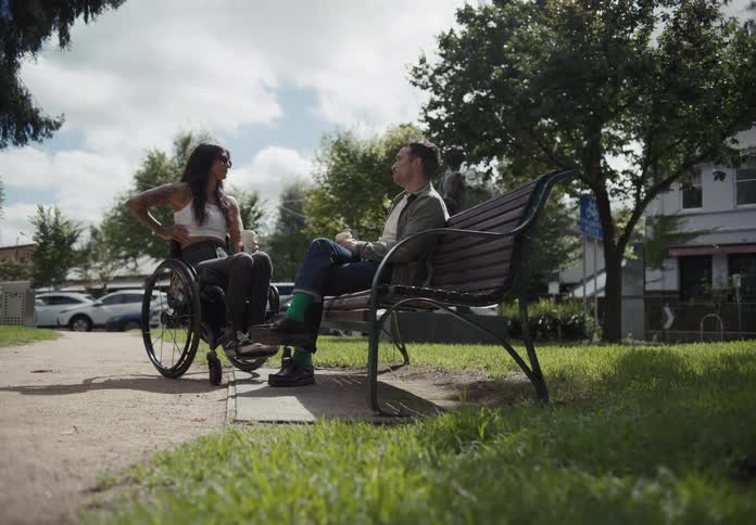 Man sitting and talking with a woman in a wheelchair in an outdoor setting