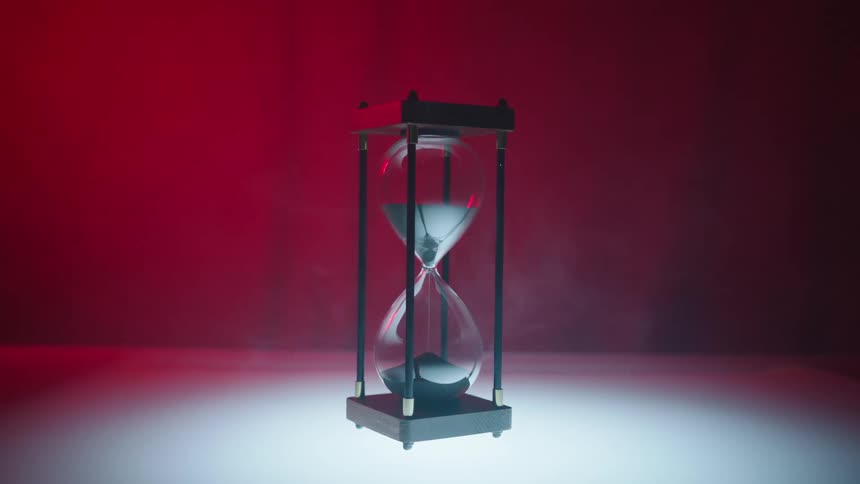 Time bulb with metallic sand falling on a red background