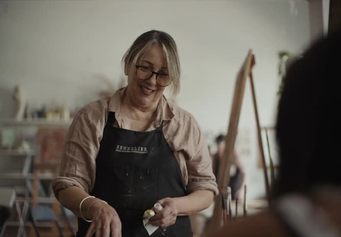 Female painter assisting another woman with paints and palettes