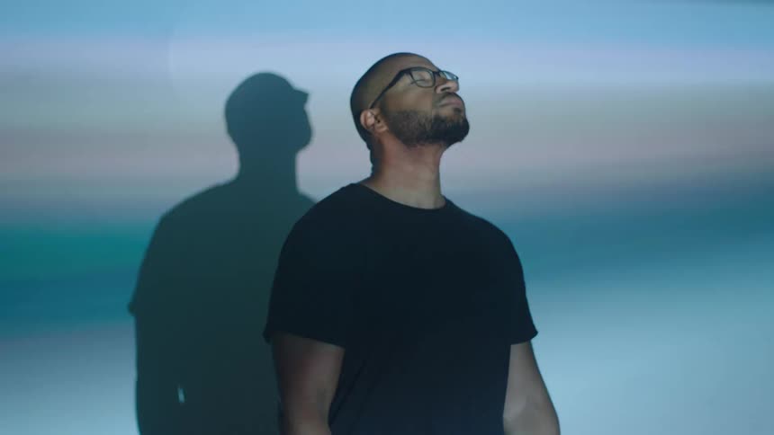 A man stands against the wall indoor facing flashing lights