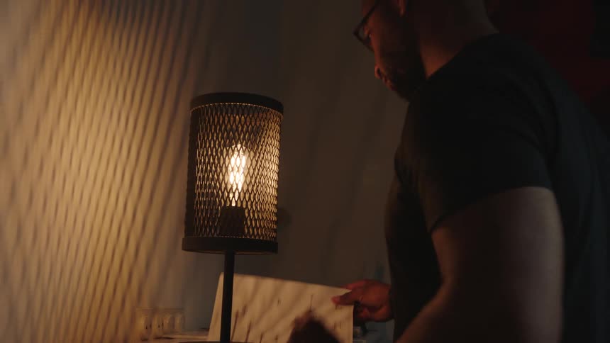 A lamp is lit as a man picks up the book