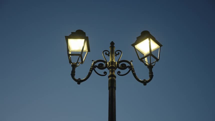 A street lamp with two lanterns is shining in the dark blue sky