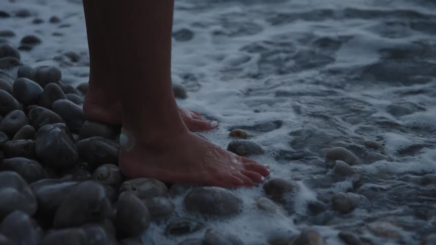 Closeup of a womans feet under the rocks with waves at the shore of the sea