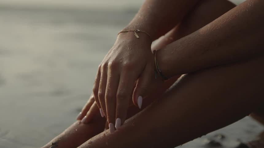 Jewelryadorned hands on knees with a blurred water backdrop