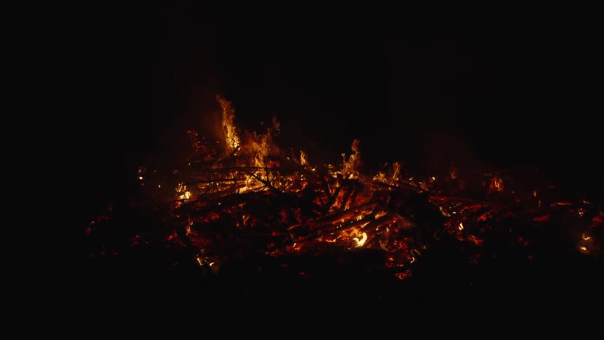 A bonfire that is burning a lot of kindling on a dark night