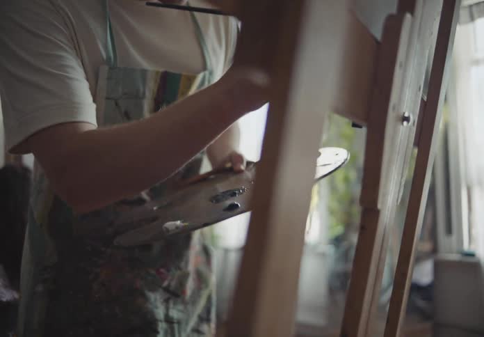 A painter holding a paint pallet and dipping the paint brush into paint