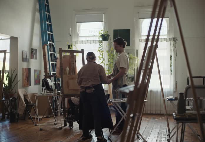 Artists talk about paintings in a room during the day