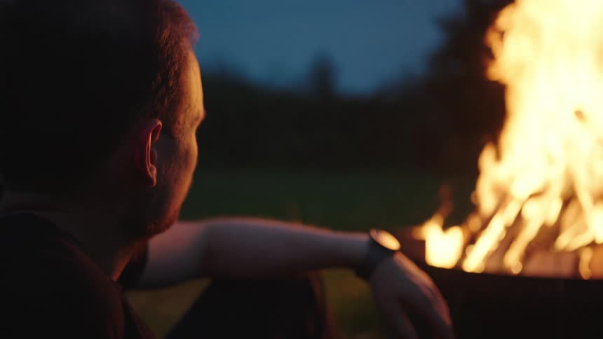 A man is sitting by the campfire