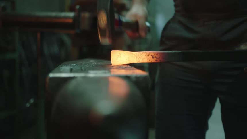 A person hammering on a hot glowing piece of metal in a shop