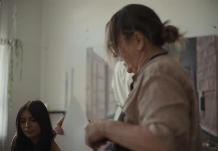 Woman assisting a person in a wheelchair with a painting canvas inside a room