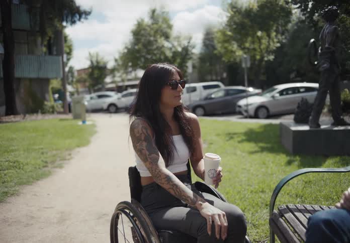 Tattooed woman sitting on a wheelchair talking to a friend in the park