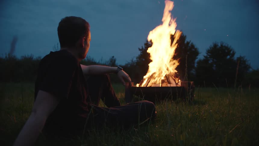 Man sitting on a lawn in front of a campfire at night