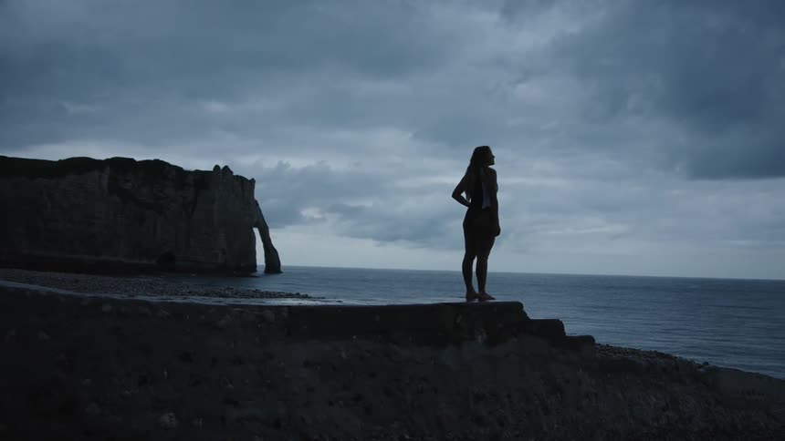 Silhouette of a woman on top of a rock by the sea on a cloudy morning