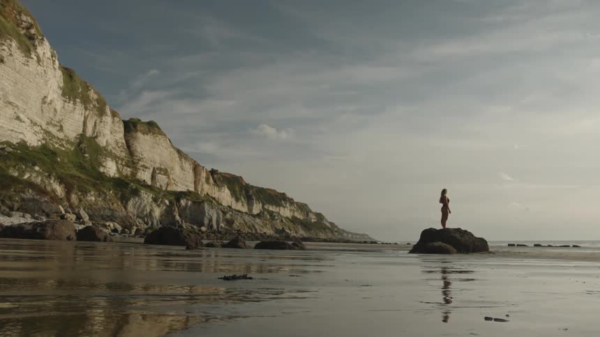A clip of a female standing on a rock by the shore