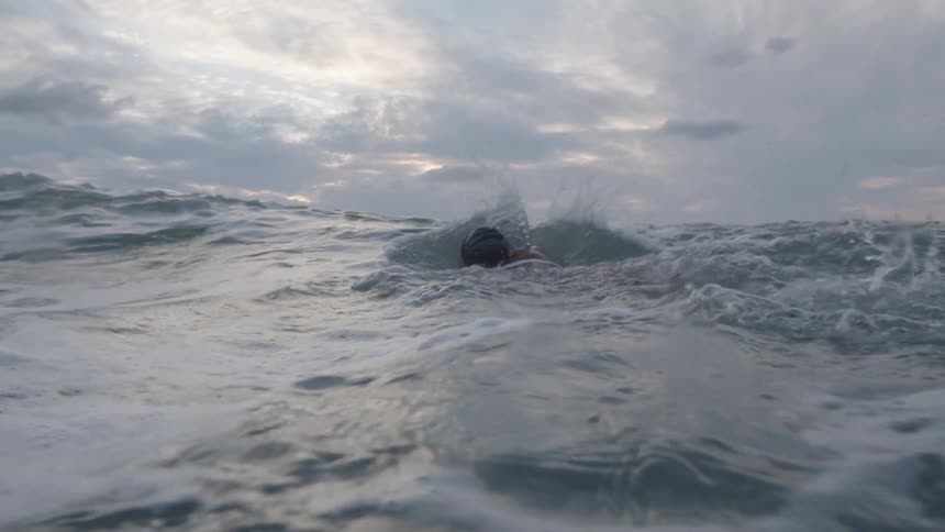 Woman swimming towards the tide on a beach on a cloudy morning